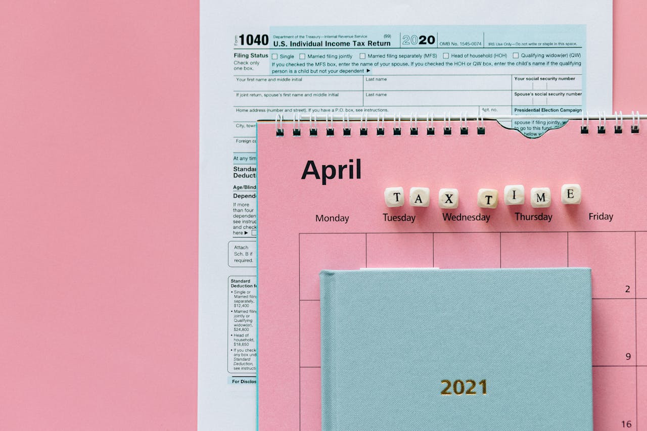 Flat lay image of tax forms, calendar, and tax time reminder on a pink background.