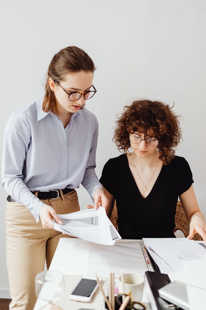 Two women working together, analyzing financial documents in an office setting.